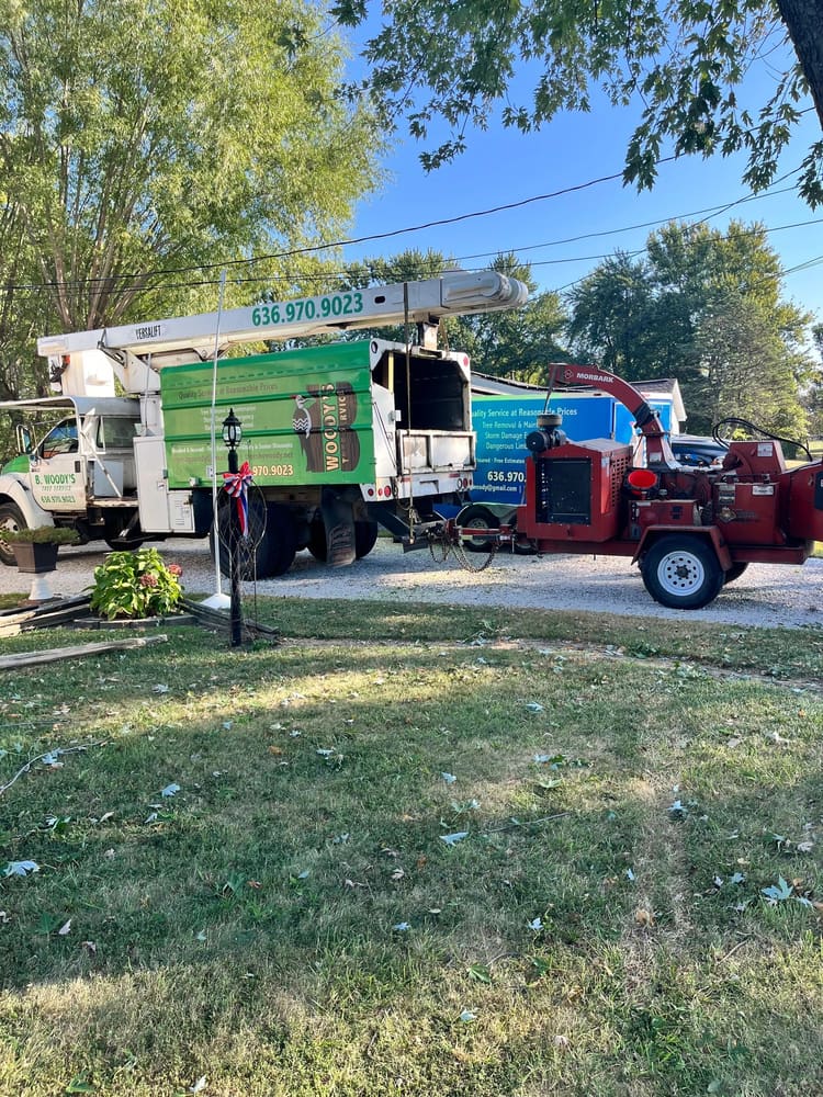 B. Woody's green bucket truck and red chipper at a residential job site